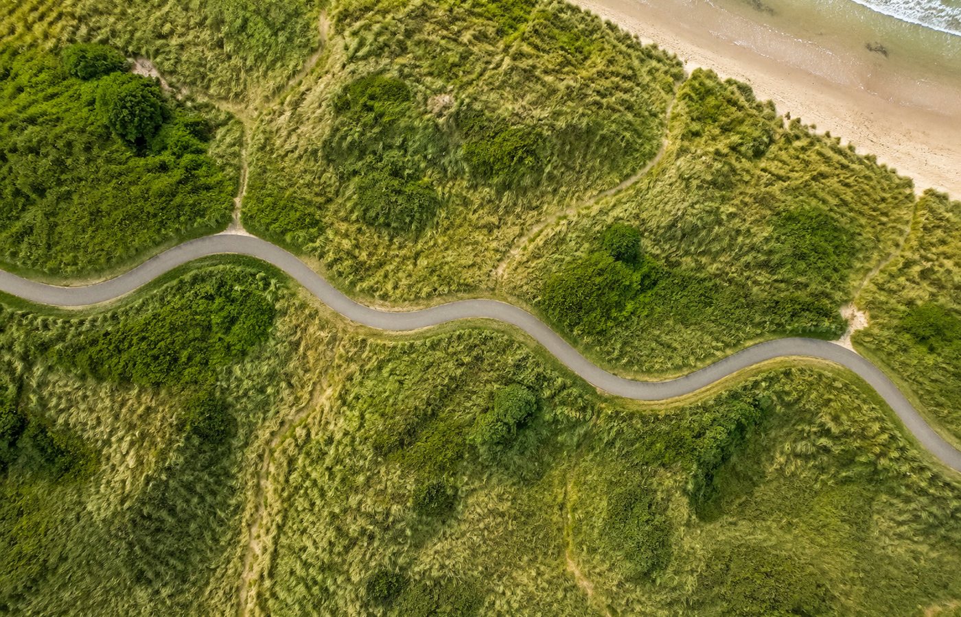 Luchtfoto recht van boven van een smal fietspad dat door groene duinen slingert